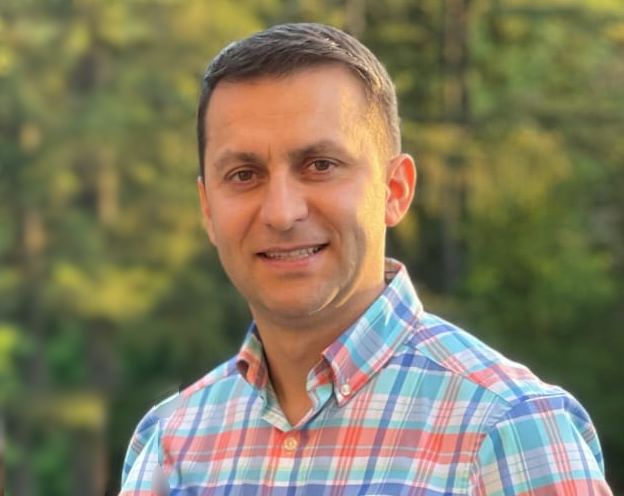 Johnny Sas founder and owner of Creative Floors Inc Aurora, Illinois. A man smiling, wearing a plaid shirt with red, blue, and white colors, outdoors with trees in the background. 