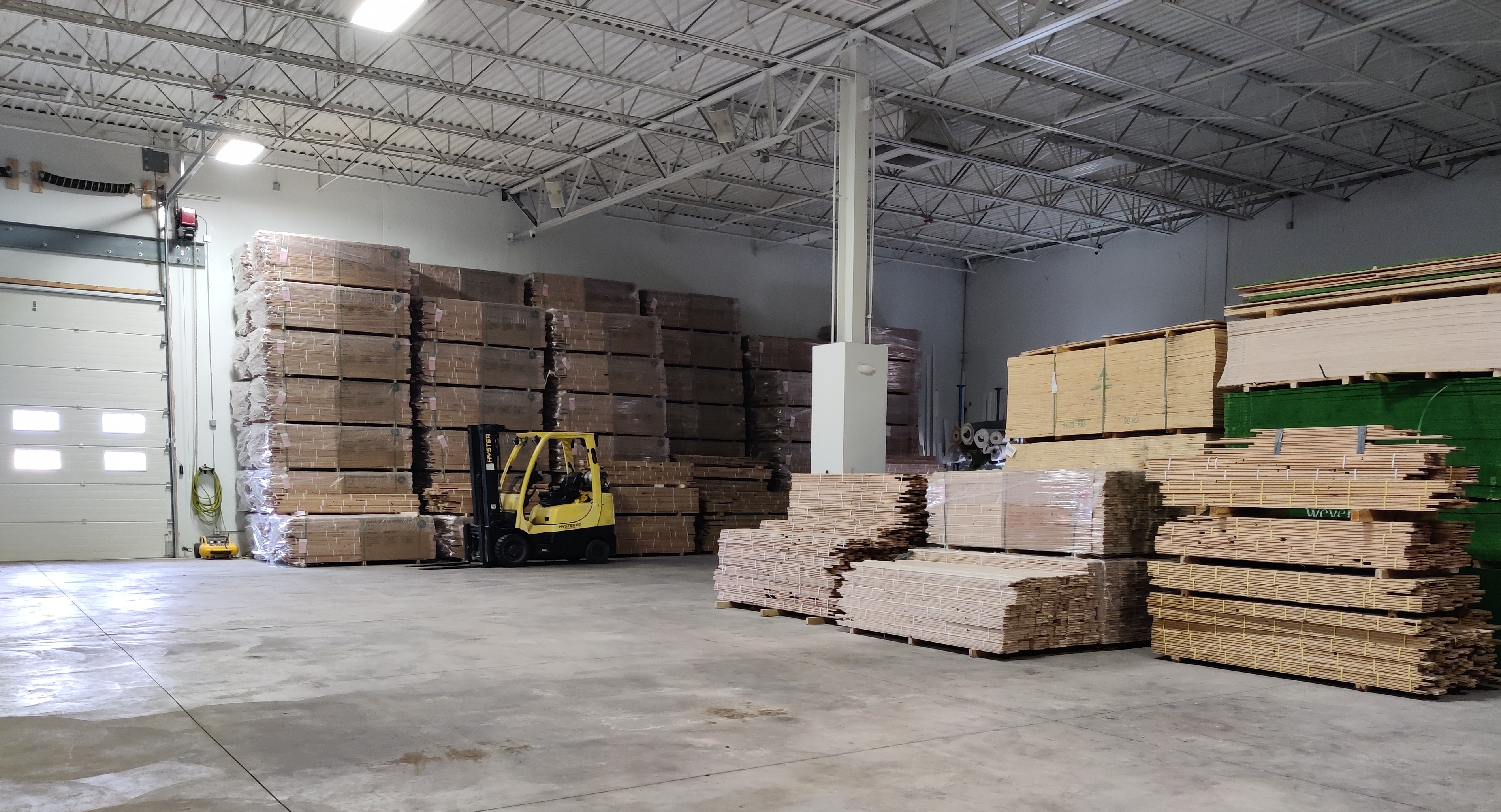 A spacious Creative Floors Inc warehouse in Aurora, with tall stacks of wood and a yellow forklift in use. 